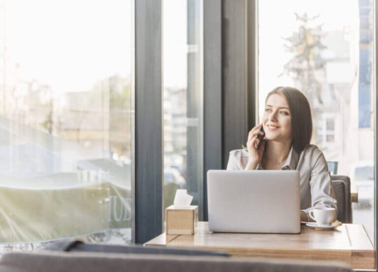 Dans un café-restaurant, une cliente est assise à une table près de grandes fenêtres vitrées offrant une belle luminosité entrante.