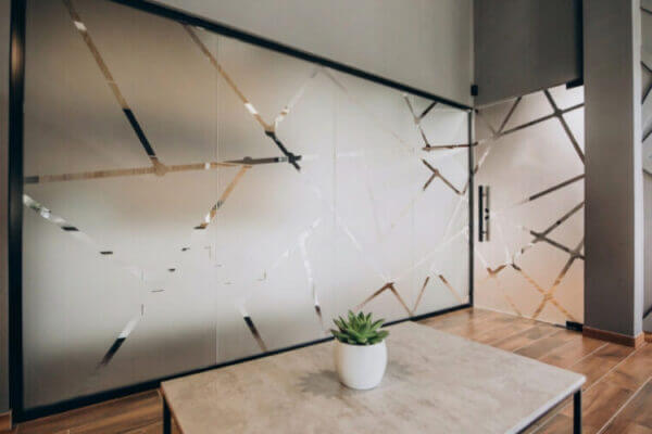 Dans des locaux professionnels, gros plan sur une paroi et une porte vitrées décorées d’un film adhésif opaque avec une vingtaine de lignes multidirectionnelles.