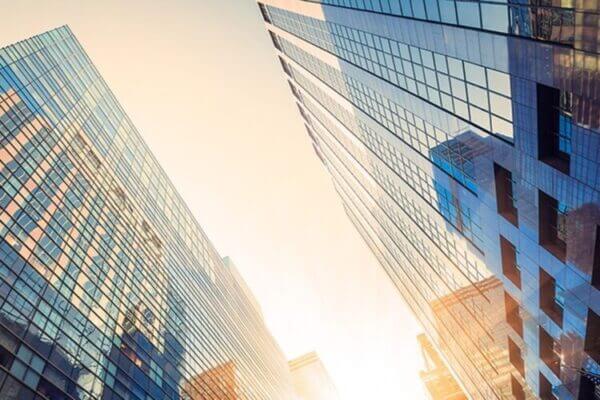 Vue en contre plongée sur de grands immeubles modernes aux façades vitrées, baignés par un soleil éblouissant.