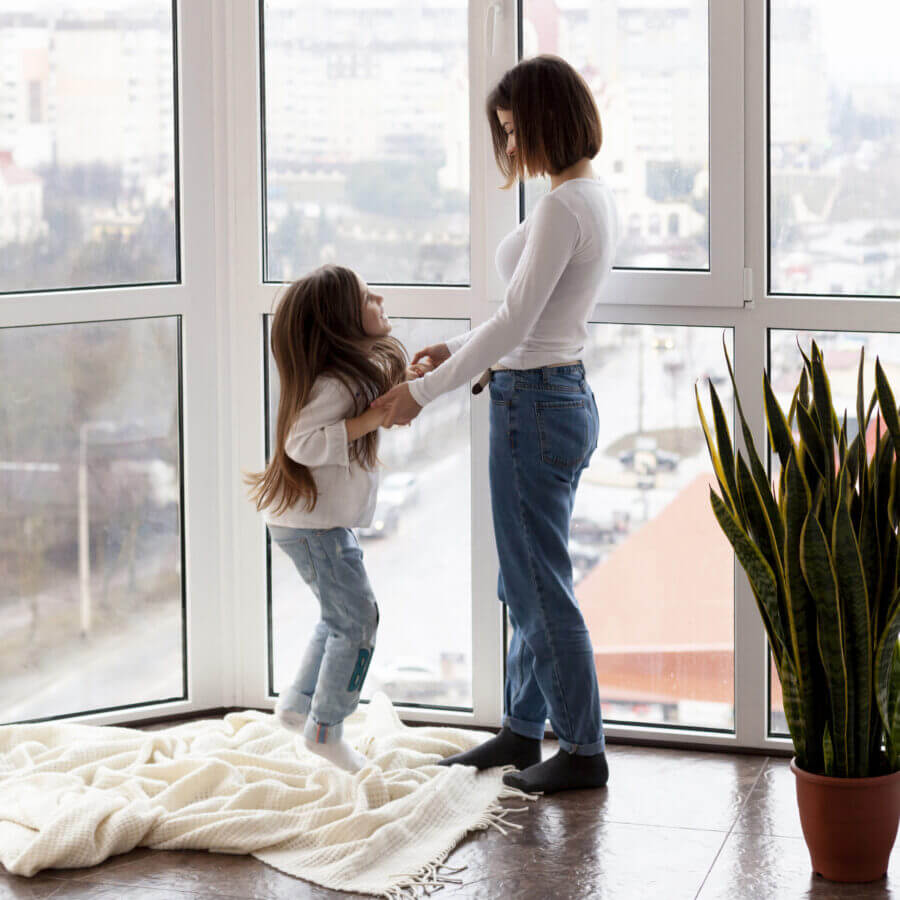 Une mère et sa fille se tiennent la main et s’amusent en toute sérénité près des fenêtres protégées de leur appartement.