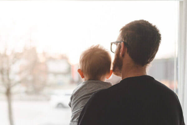 Dos à la caméra, un père et son bébé regardent la rue à travers la fenêtre sécurisée de leur maison.