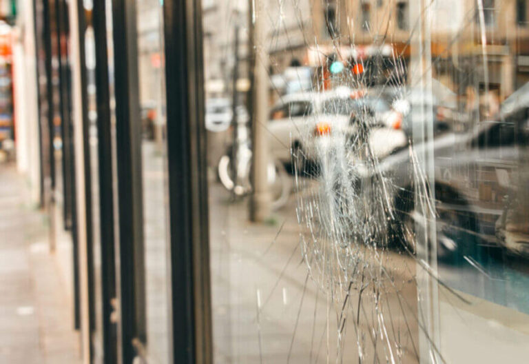 Vue extérieure d’un commerce situé en centre-ville avec une vitrine fissurée et maintenue par un film anti-effraction.